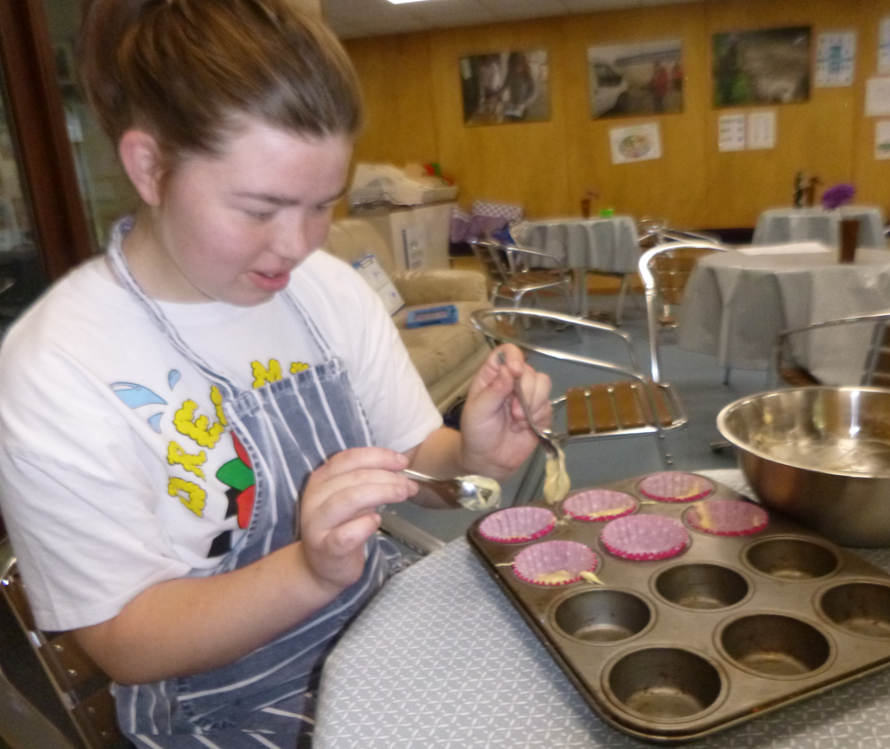 female student placing cake batter into cupcake tin